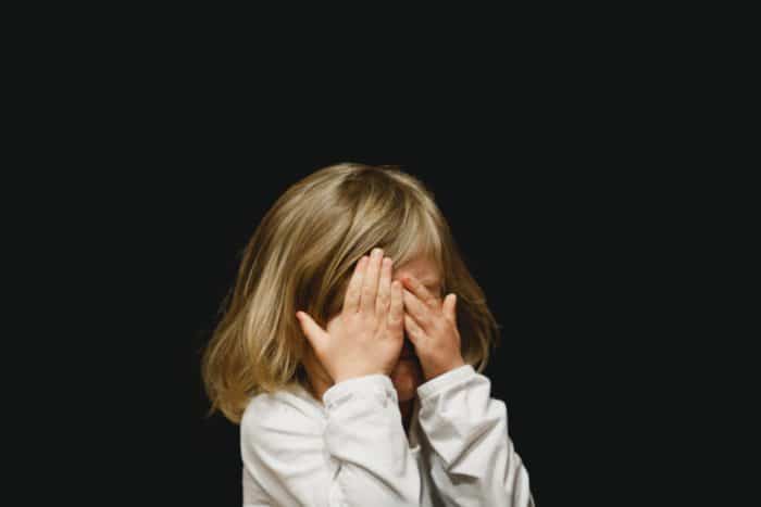 Tunteikas lapsi piilottaa kasvonsa käsien taakse
