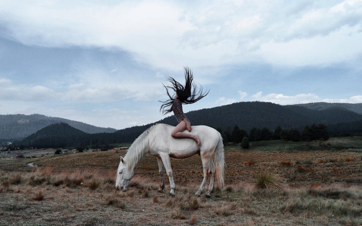 Nainen ratsastaa valkealla hevosella