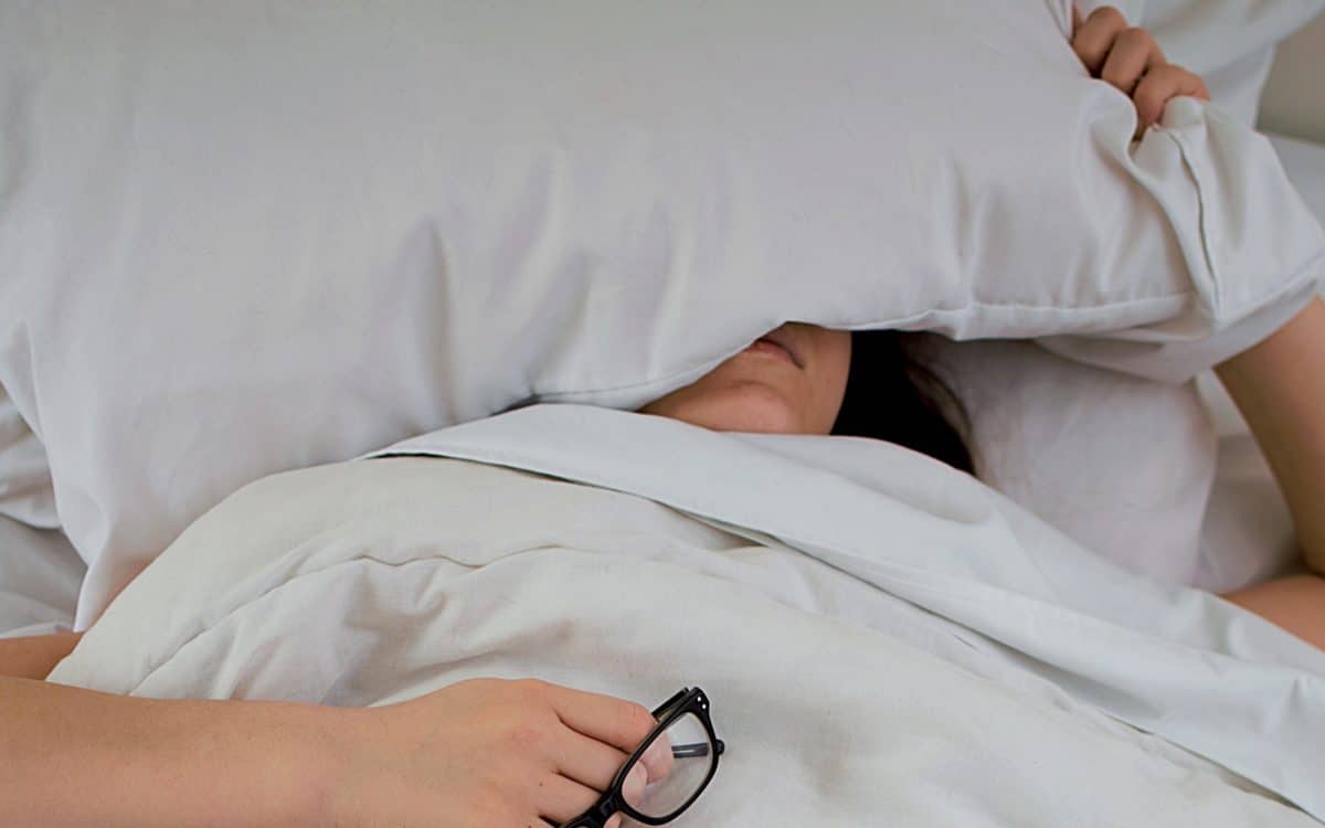 Nainen sängyssä pää tyynyn alla