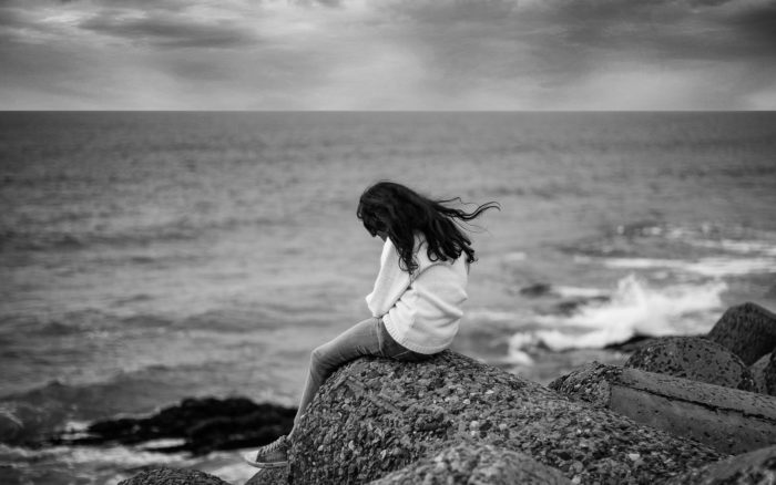 Mustavalkoinen kuva naisesta yksin myrskyisellä rannalla