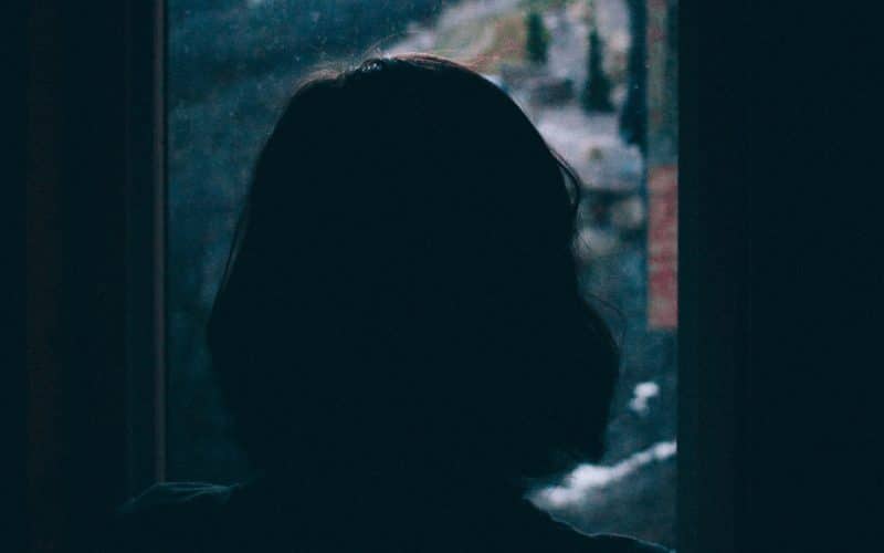 nainen katsoo pimeässä ikkunasta ulos
