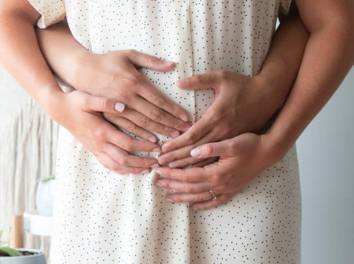 pariskunta kädet naisen raskausvatsalla